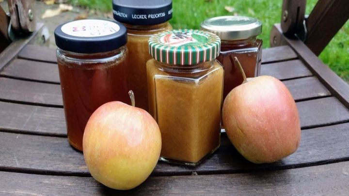 Eingemachte Bratapfelgelee und &Auml;pfel stehen auf einem Holztisch in einer gr&uuml;nen Gartenumgebung.