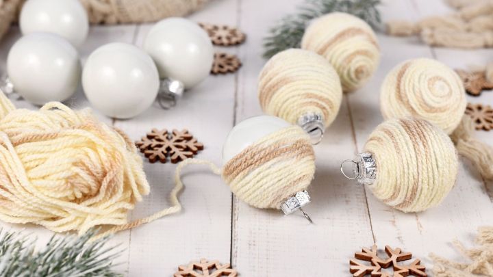 Bunte Weihnachtskugeln aus Wolle liegen auf einem Tisch, umgeben von Holz- und Schneeflockendekorationen.
