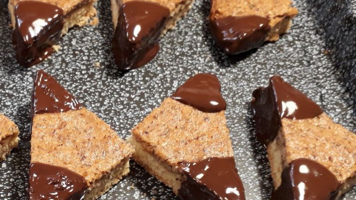 Auf einem schwarzen Blech sind mehrere Nussecken angerichtet, die mit Schokolade &uuml;berzogen sind und appetitlich wirken.