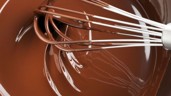 Dunkle Schokolade wird mit einem Schneebesen in einer Sch&uuml;ssel verr&uuml;hrt, um eine glatte Kuvert&uuml;re zu erzeugen.