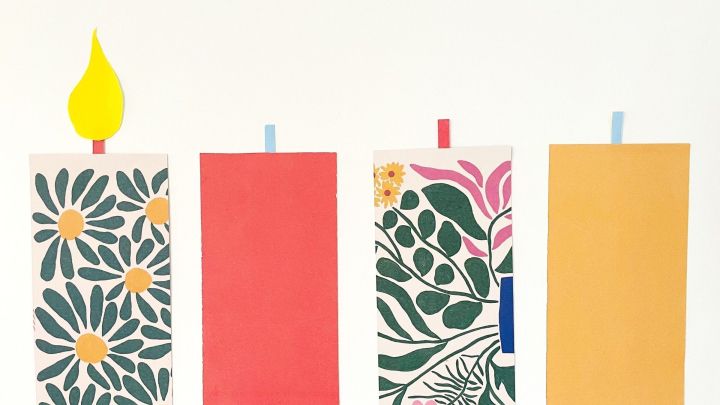 Ein adventliches Gesteck zeigt beleuchtete Kerzen, die kindgerecht und dekorativ mit bunten Mustern gestaltet sind.