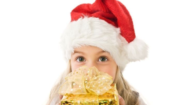 Ein Kind mit rotem Weihnachtsmann-Hut h&auml;lt ein Geschenk mit goldenem Geschenkband und &uuml;berrascht in festlicher Stimmung.