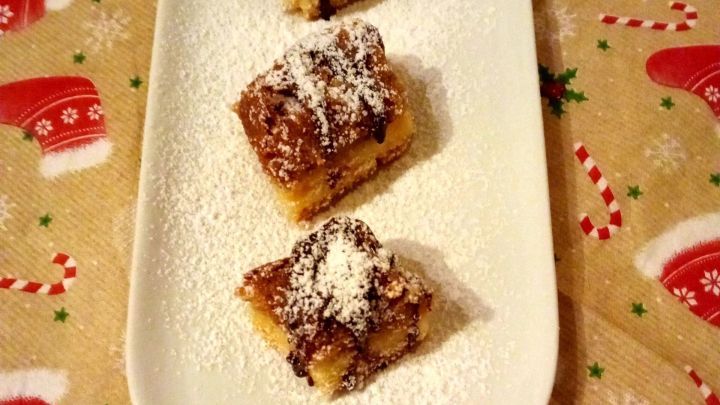 Drei Nussecken mit Puderzucker und Schokolade liegen auf einem wei&szlig;en Teller, umgeben von festlichem Weihnachtsgeschirr.