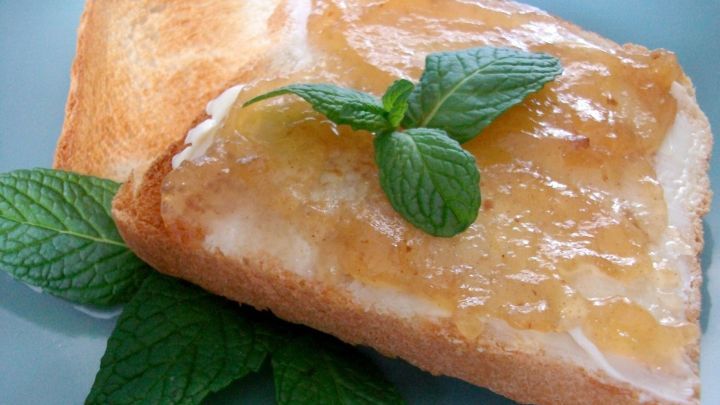 Ein St&uuml;ck Toast mit Apfel-Zimt-Rum-Marmelade ist mit frischen Minzbl&auml;ttern dekoriert und auf einem blauen Teller angerichtet.