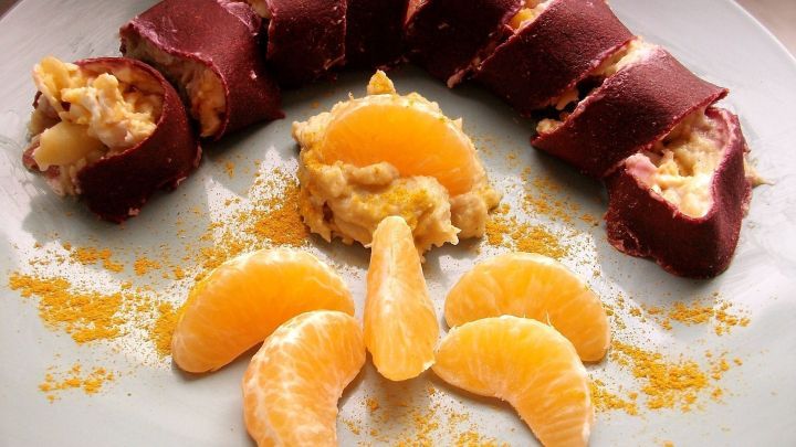 Rosenkohl- und Rote-Bete-Tortillas sind kunstvoll auf einem Teller angerichtet, umgeben von frischen Mandarinenst&uuml;cken.