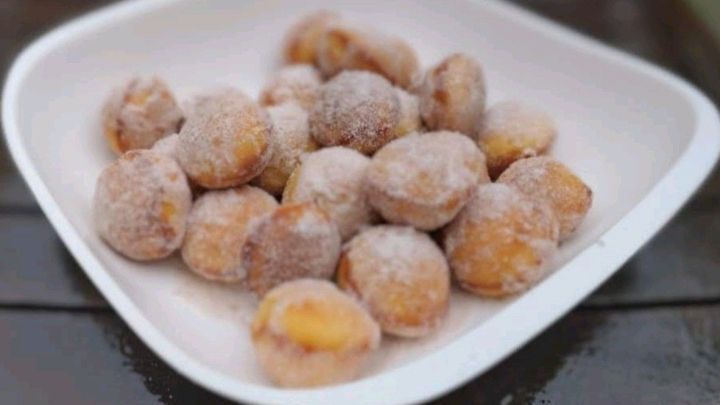 Kleine Quarkb&auml;llchen auf einem wei&szlig;en Teller, zuckerbestreut und appetitlich, liegen auf einem h&ouml;lzernen Tisch.