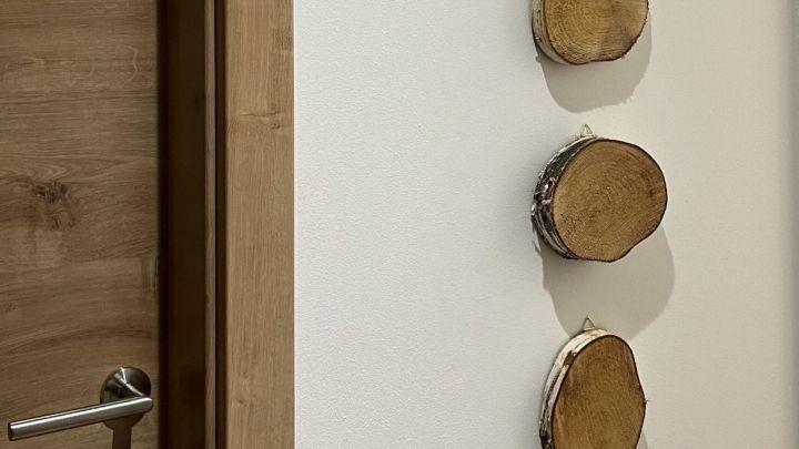 Drei Birkenscheiben h&auml;ngen an einer wei&szlig;en Wand neben einer Holzfarbent&uuml;r und verleihen dem Raum nat&uuml;rlichen Charme.