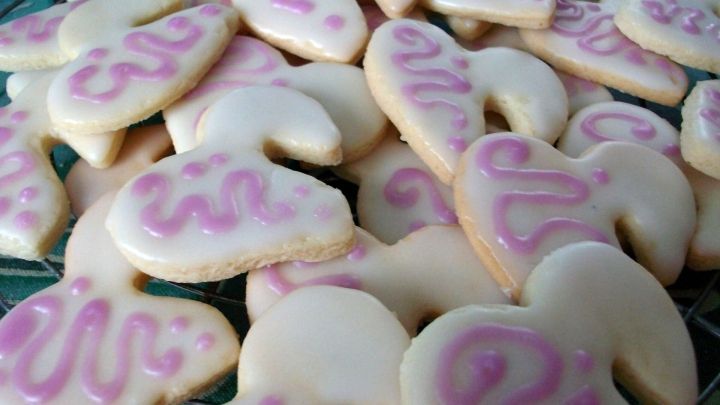 Zuckerguss-tropfen liegen auf bunten Keksen, die frisch dekoriert auf einem Gitterrost abgek&uuml;hlt werden.