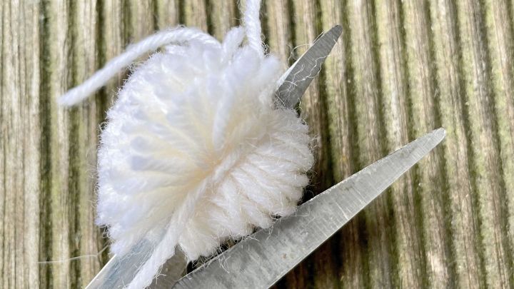 Mit einer Schere wird die zusammengezogene Wolle an den beiden Seiten aufgeschnitten.