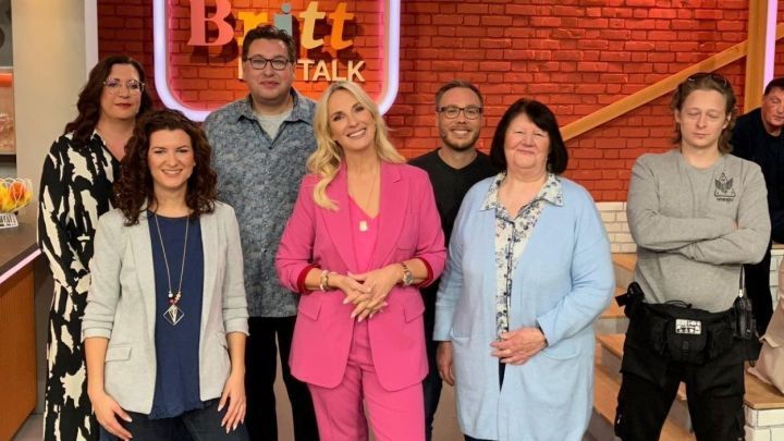 Eine Gruppe von sieben Menschen steht l&auml;chelnd im Studio vor einer roten Backsteinwand mit dem Schriftzug &bdquo;Britt TALK&ldquo;.