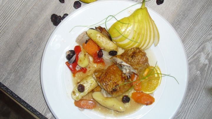 H&auml;hnchenschlegel liegt auf einem bunten Gem&uuml;sebett mit fruchtiger So&szlig;e, umgeben von Obst und dekorativen Beilagen.