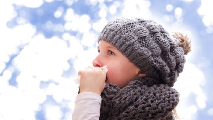 Ein kleines M&auml;dchen in einem warmen, grauen Wollm&uuml;tze und Schal schn&auml;uzt sich in einer kalten, frostigen Umgebung.
