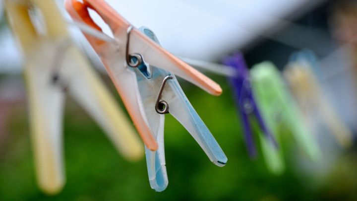 Bunte W&auml;scheklammern halten eine W&auml;scheleine in einem Garten, was auf eine typische Alltagsszene zwischen Weihnachten und Silvester hinweist.