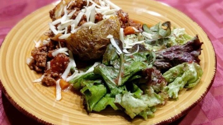 Ein Teller mit Bolognese und Backkartoffeln ist angerichtet, umgeben von frischem Salat, auf einem gestreiften Tischcloth.