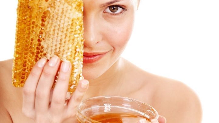 Eine Frau h&auml;lt eine Wabe in der einen Hand und eine Sch&uuml;ssel mit Honig in der anderen, l&auml;chelnd vor einem hellen Hintergrund.