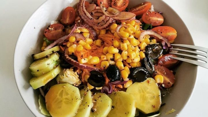 Ein bunter Salat mit Gurken, Tomaten, Mais und Oliven wird appetitlich in einer Sch&uuml;ssel angerichtet, um gesund zu essen.