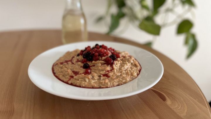 Porridge wird mit frischen roten und schwarzen Beeren garniert und steht auf einem Holztisch vor einer Pflanze.