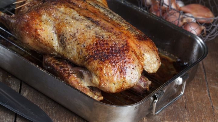 Eine goldbraun gebratene Ente liegt auf einem Rost in einer Metallsch&uuml;ssel, umgeben von einem rustikalen Holzuntergrund.
