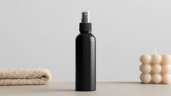 Ein schwarzer Spr&uuml;hbeh&auml;lter steht auf einem Tisch neben einem Handtuch und einer dekorativen Kerze.