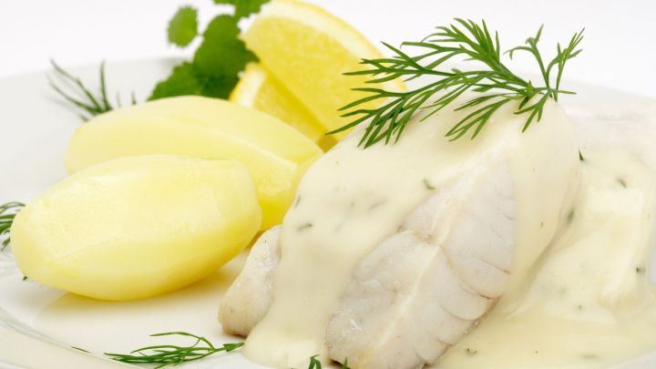 Ein saftiger Seelachs liegt auf einem Teller, &uuml;berzogen mit Zitronen-Schnittlauch-So&szlig;e, begleitet von gekochten Kartoffeln und Zitronenscheiben.