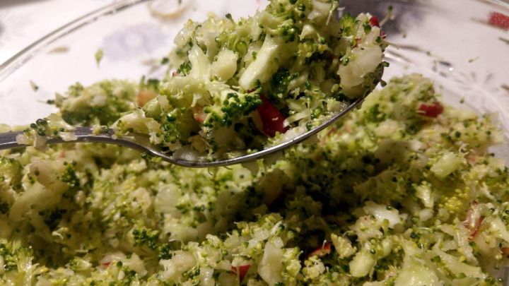 Ein L&ouml;ffel mit einem frischen Brokkoli-Apfel-Salat wird gehalten, um &uuml;ber eine Sch&uuml;ssel mit Salat zu schauen.