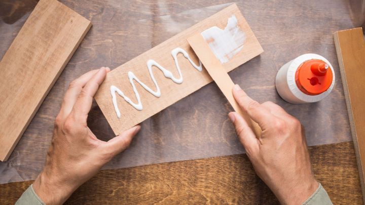 Ein Handwerker tr&auml;gt wei&szlig;em Kleber mit einem Spachtel auf ein Holzst&uuml;ck auf, um es zu verbinden.