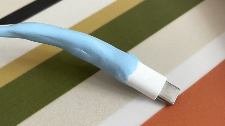 Ein Kabel ist mit blauer Reparaturknete ummantelt, um einen Wackelkontakt zu beheben, auf einem gestreiften Untergrund.