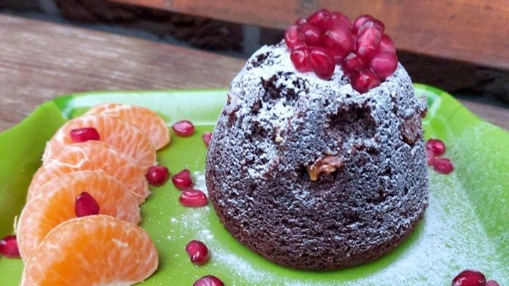 Schokoladenkuchen steht auf einem gr&uuml;nen Teller, dekoriert mit Mandarinenst&uuml;cken und Granatapfelkernen in nat&uuml;rlichem Licht.