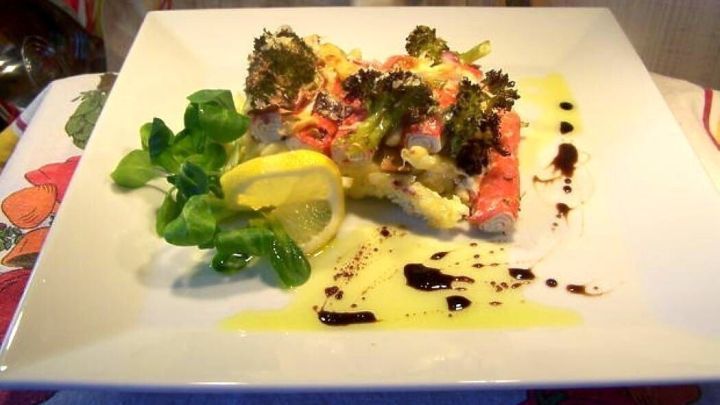 Ein ansprechend dekorierter Brokkoli-Auflauf mit Surimi und Zitrone pr&auml;sentiert sich auf einem wei&szlig;en Teller, umgeben von frischem Gem&uuml;se.