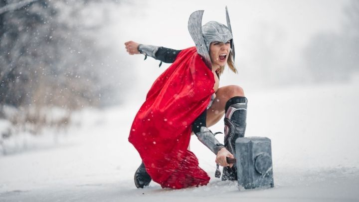 Eine Kriegerin im roten Umhang zieht mit Entschlossenheit ihren Hammer durch den Schneefall in einer winterlichen Landschaft.