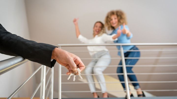 Ein Schl&uuml;sselbund wird einem erfreuten Paar &uuml;berreicht, das l&auml;chelnd und jubelnd in einer Wohnung steht.