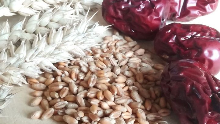 Weizen und rote Datteln liegen auf einem Holzbrett, bereit zur Zubereitung von Weizentee zur F&ouml;rderung des Schlafs.