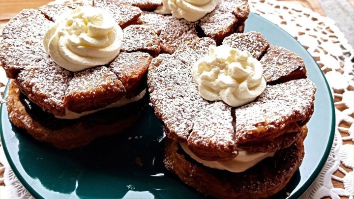 Drei frisch gebackene Friesent&ouml;rtchen, geschichtet mit Sahne und Puderzucker, auf einem gr&uuml;nen Teller pr&auml;sentiert.