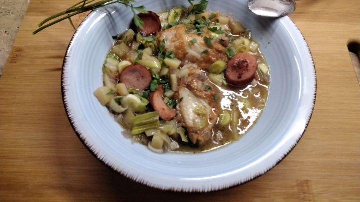 Eine Sch&uuml;ssel mit Reste-Suppe, gef&uuml;llt mit Gem&uuml;se, H&uuml;hnerteilen und W&uuml;rstchen, steht auf einem Holzbrett.