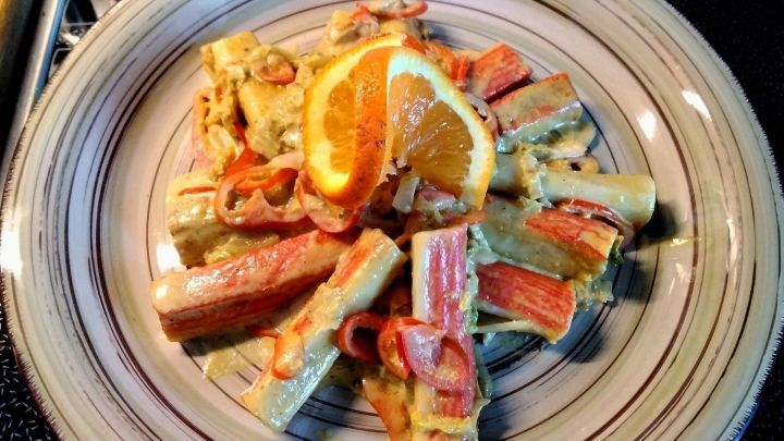 Eine warme und cremige Chinakohl-Pfanne mit Surimi, dekoriert mit frischen Orange- und Zwiebelstreifen auf einem Teller.