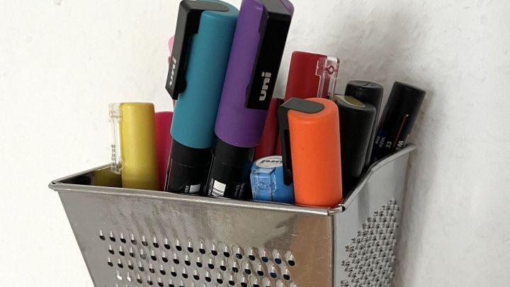 Ein Stiftehalter aus einer alten Reibe steht an der Wand und h&auml;lt bunte Stifte und Marker, kreativ und praktisch.