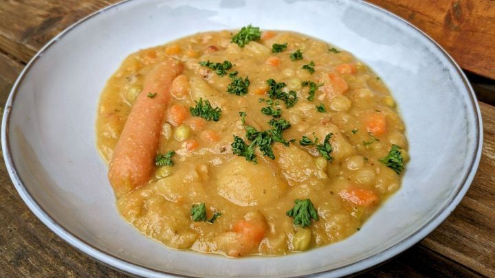 Eine dampfende Sch&uuml;ssel Pille Palle Suppe zeigt eine cremige Mischung aus Karotten, Erbsen und Petersilie, serviert auf einem Holzuntergrund.