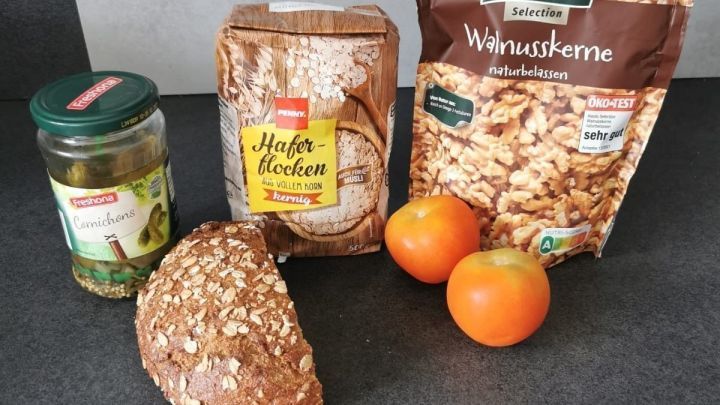 Haferflocken und Waln&uuml;sse liegen neben frischem Brot und Orangen auf einem dunklen Tisch, bereit f&uuml;r ein g&uuml;nstiges Fr&uuml;hst&uuml;ck.