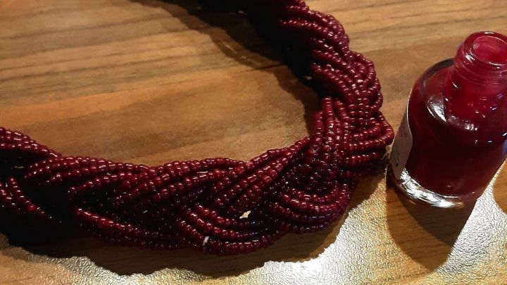 Eine rote Kette liegt auf einem Holztablett, w&auml;hrend daneben eine Flasche Nagellack steht, bereit zum Ausbessern.