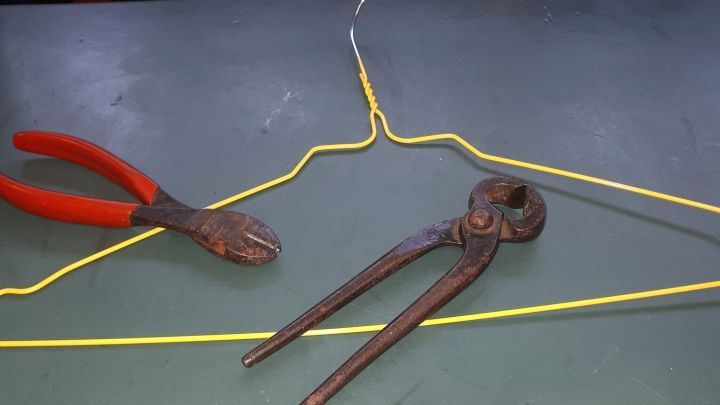 Ein gelber Drahtb&uuml;gel liegt auf einem Tisch, w&auml;hrend Zangen daneben liegen, bereit zum Biegen und Schneiden.