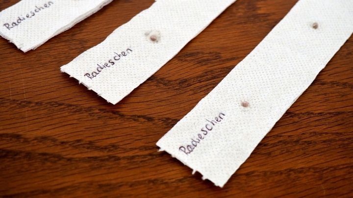 Drei wei&szlig;e Saatb&auml;nder mit beschrifteten Abst&auml;nden f&uuml;r Radieschen liegen auf einem Holztisch.
