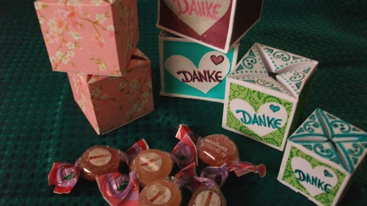 Bunte, selbstschlie&szlig;ende Bonbonschachteln stehen auf einem gr&uuml;nen Untergrund, umgeben von verschiedenen S&uuml;&szlig;igkeiten.