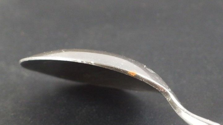 Ein L&ouml;ffel mit Flugrostflecken liegt auf einem dunklen Untergrund, wodurch die Rostflecken deutlich sichtbar werden.