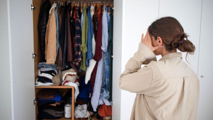 Eine Person steht vor einem &uuml;berf&uuml;llten Kleiderschrank und h&auml;lt sich frustriert die H&auml;nde vor das Gesicht.