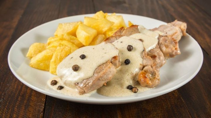 Zarte Schweinemedaillons in cremiger Meerrettichso&szlig;e liegen neben goldenen Kartoffelw&uuml;rfeln auf einem Teller.