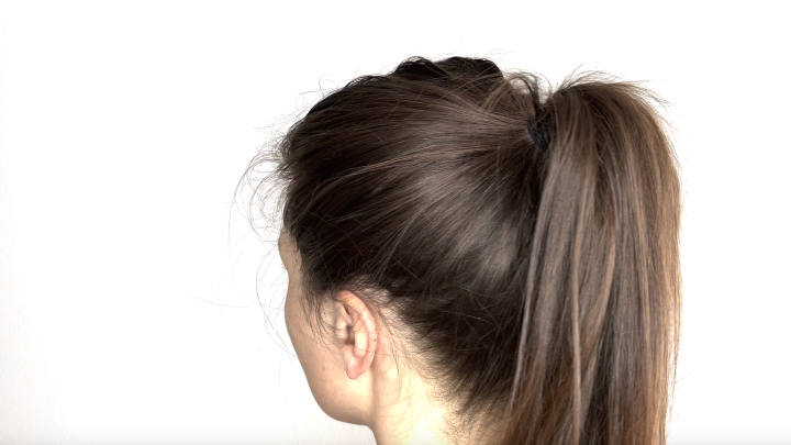 Ein volumin&ouml;ser Pferdeschwanz wird mit einem Haargummi gestylt. Die Person zeigt ihren R&uuml;cken vor wei&szlig;em Hintergrund.