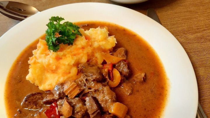 Saftiges Gulasch mit Paprika liegt appetitlich auf einem Teller, begleitet von Kartoffelbrei und einem frischen Salat.