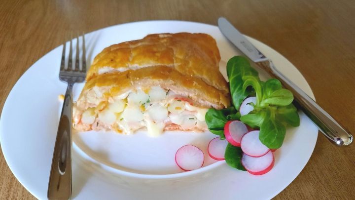 Ein knuspriger Spargel im Bl&auml;tterteig liegt auf einem wei&szlig;en Teller, umgeben von Salat und Radieschen, mit Besteck daneben.