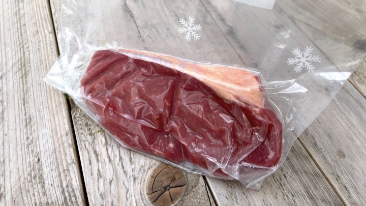 Ein vakuumierter Beutel mit Fleisch liegt auf einer Holzoberfl&auml;che, w&auml;hrend Wasser um den Beutel herum ist.