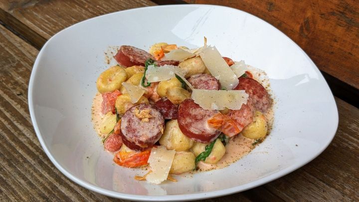 Gnocchi mit Wurst und K&auml;se sind in einer Schale angerichtet, umgeben von einem rustikalen Holzuntergrund.